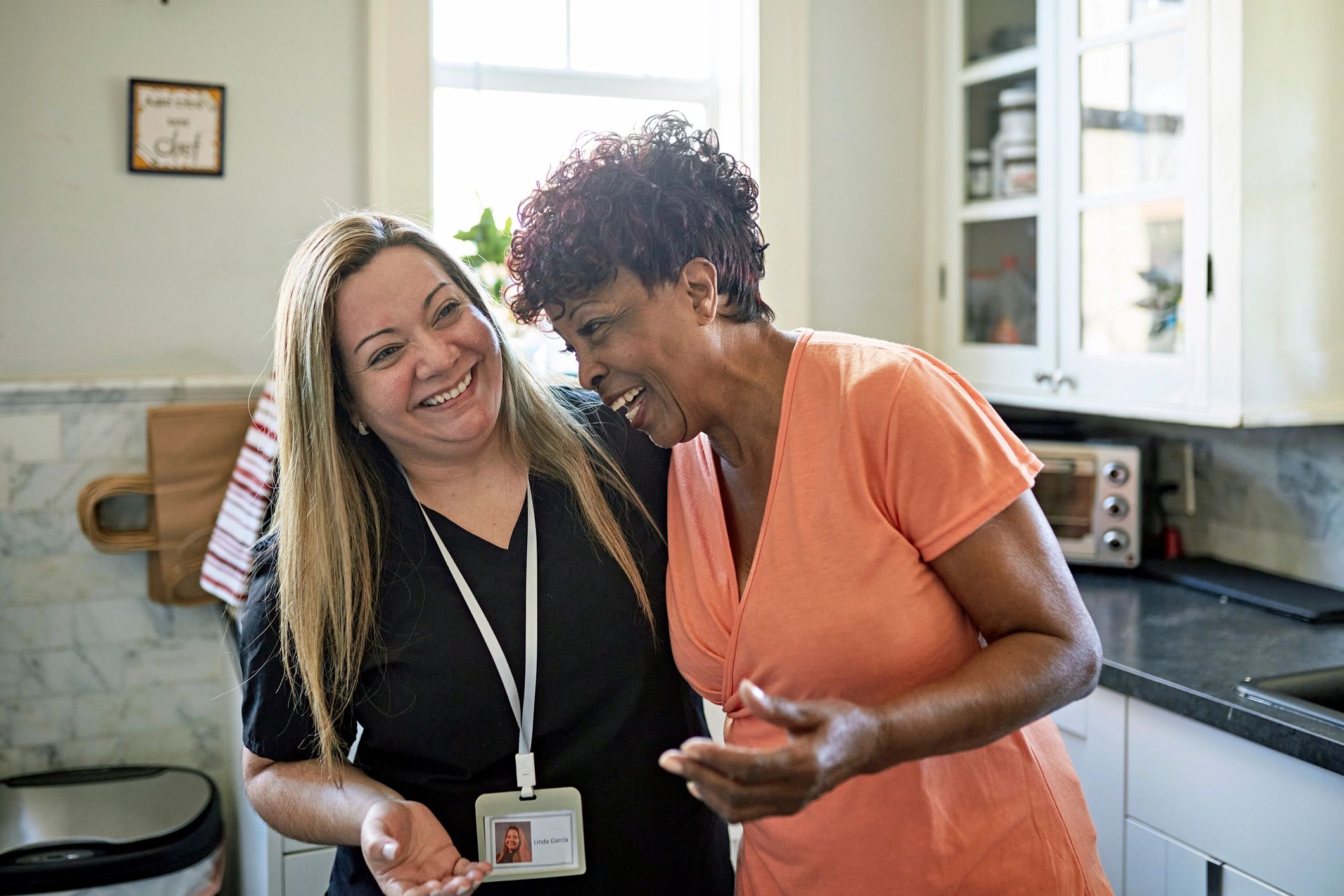 Caregiver and senior woman smiling together in a kitchen