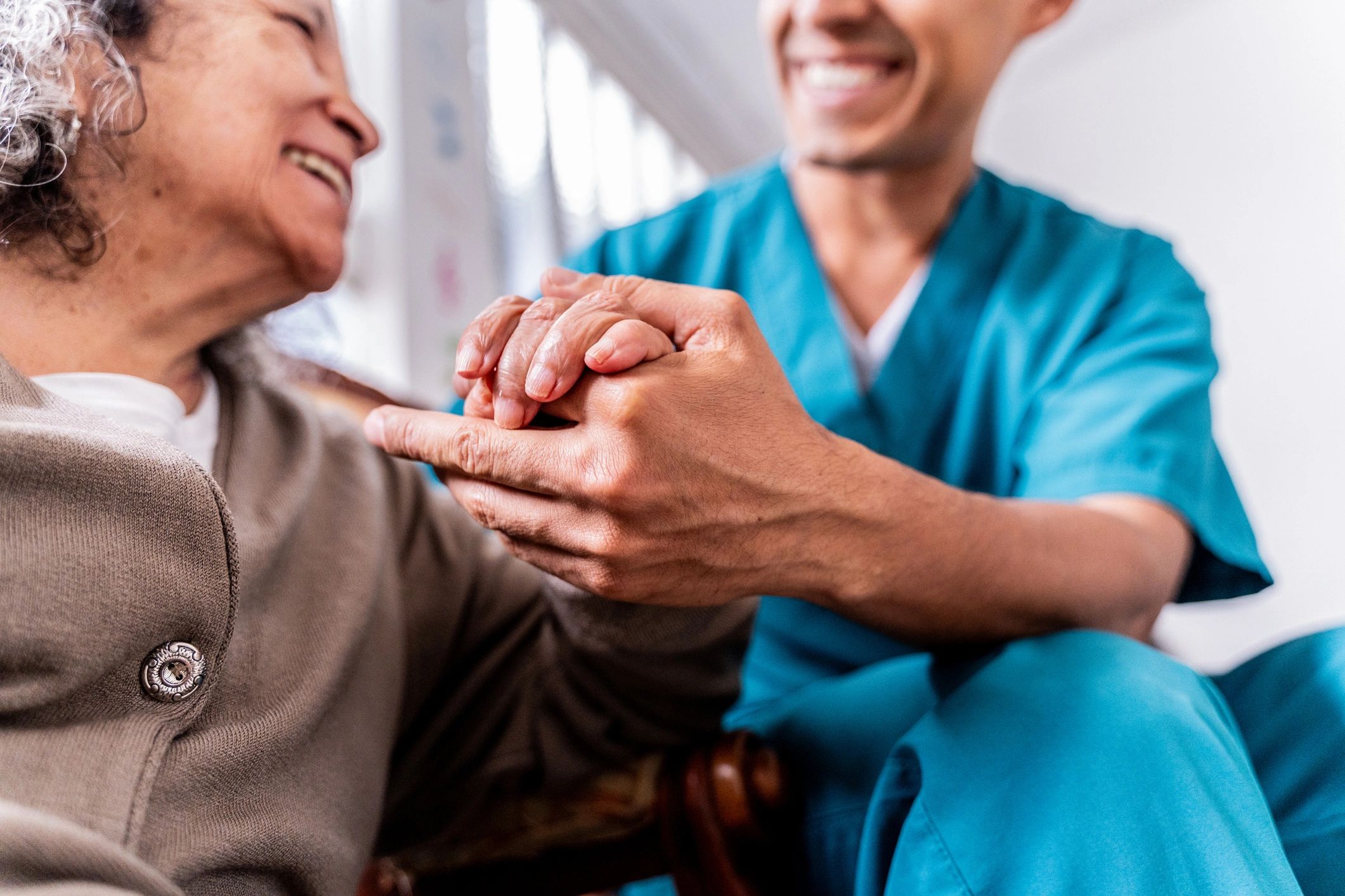 Senior woman holding a caregiver’s hands at home